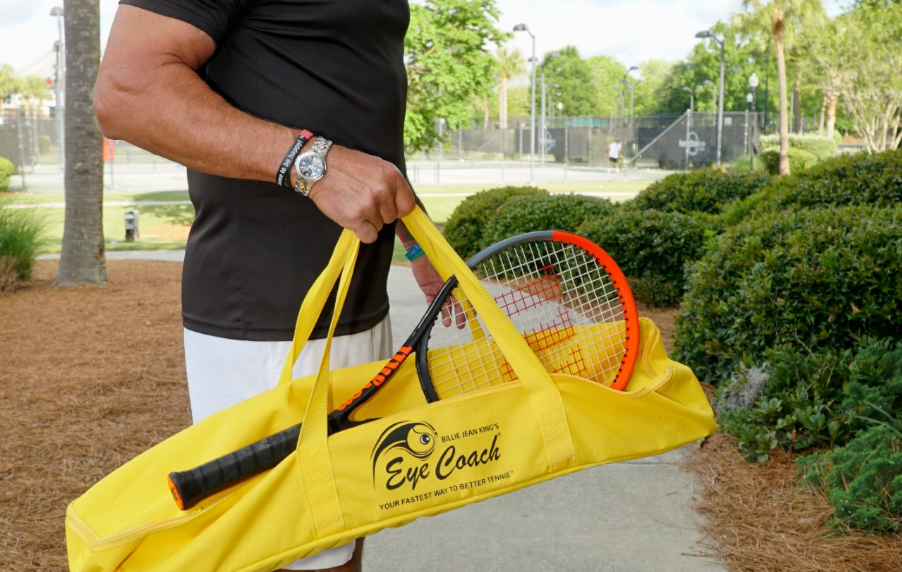 A man carrying a yellow Eye Coach tennis bag